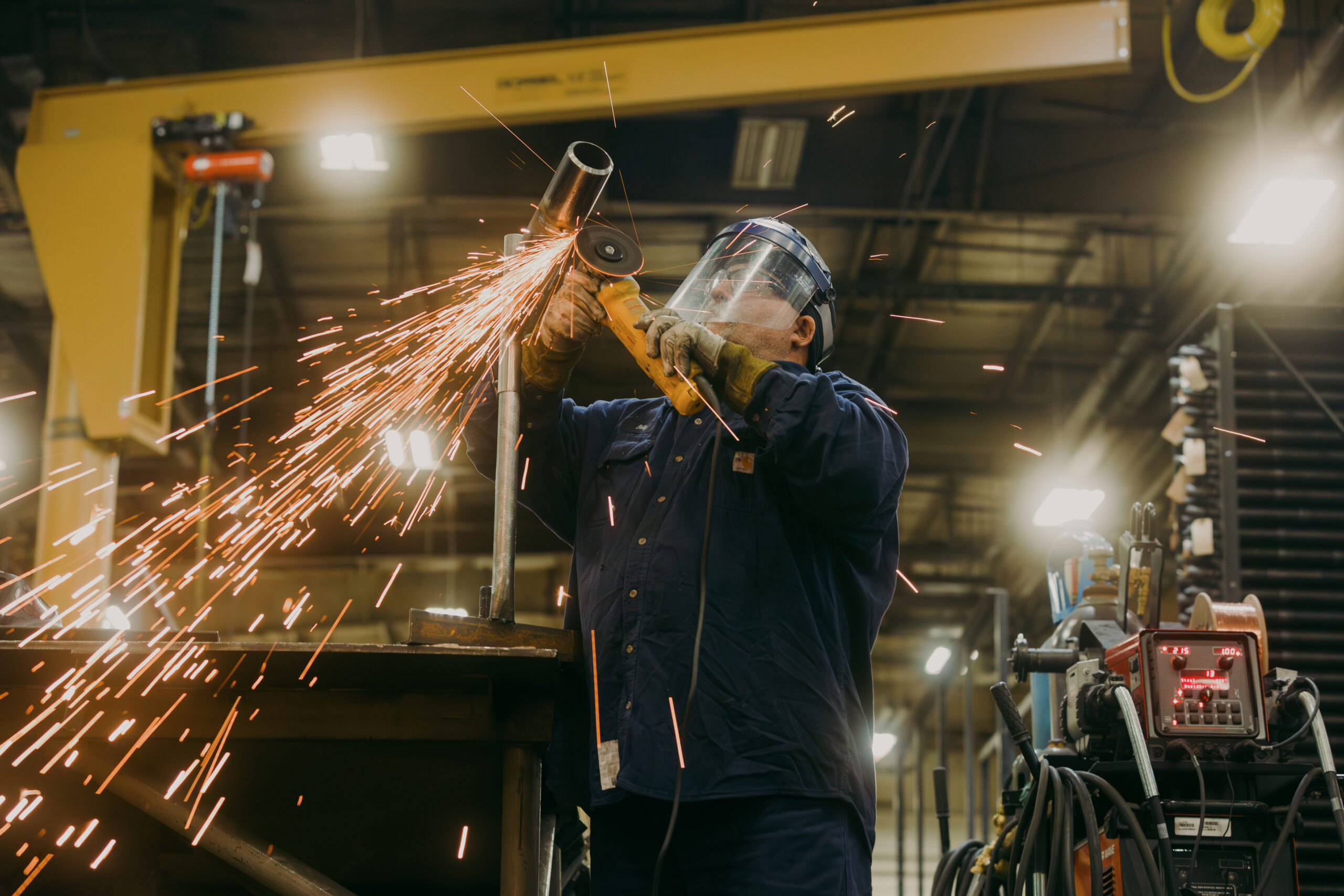 Worker welding metal with sparks flying in industrial workshop setting.