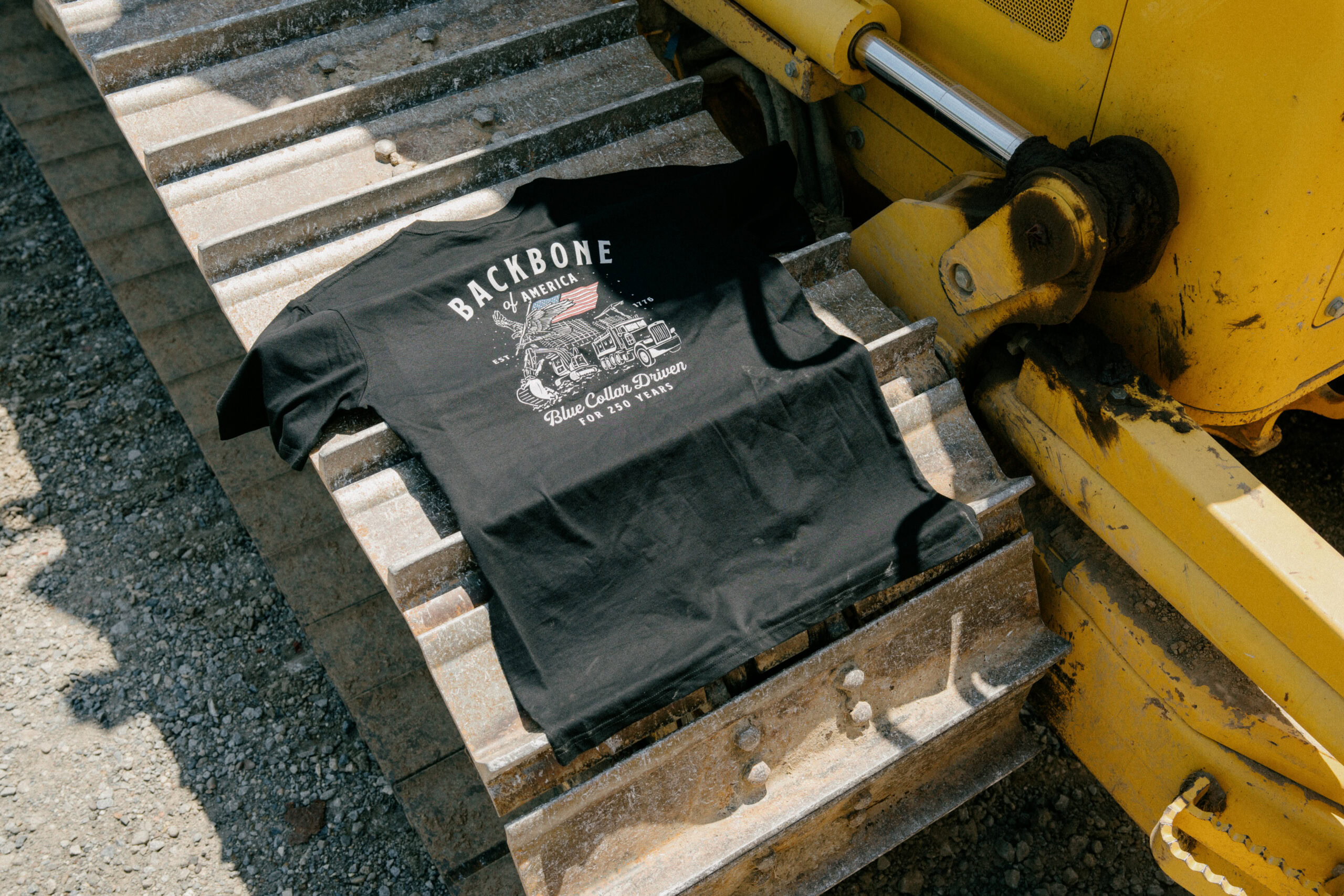 Black Cat Creative Co. T-shirt laid on railroad track with yellow machinery nearby.
