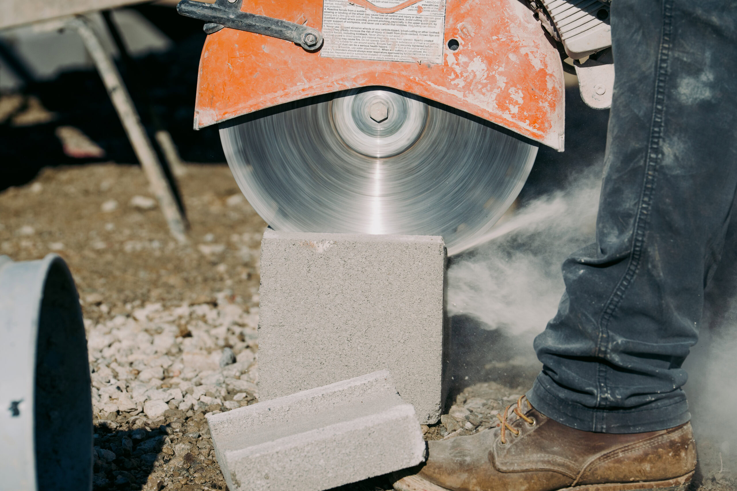 Worker using a circular saw to cut concrete block at construction site.