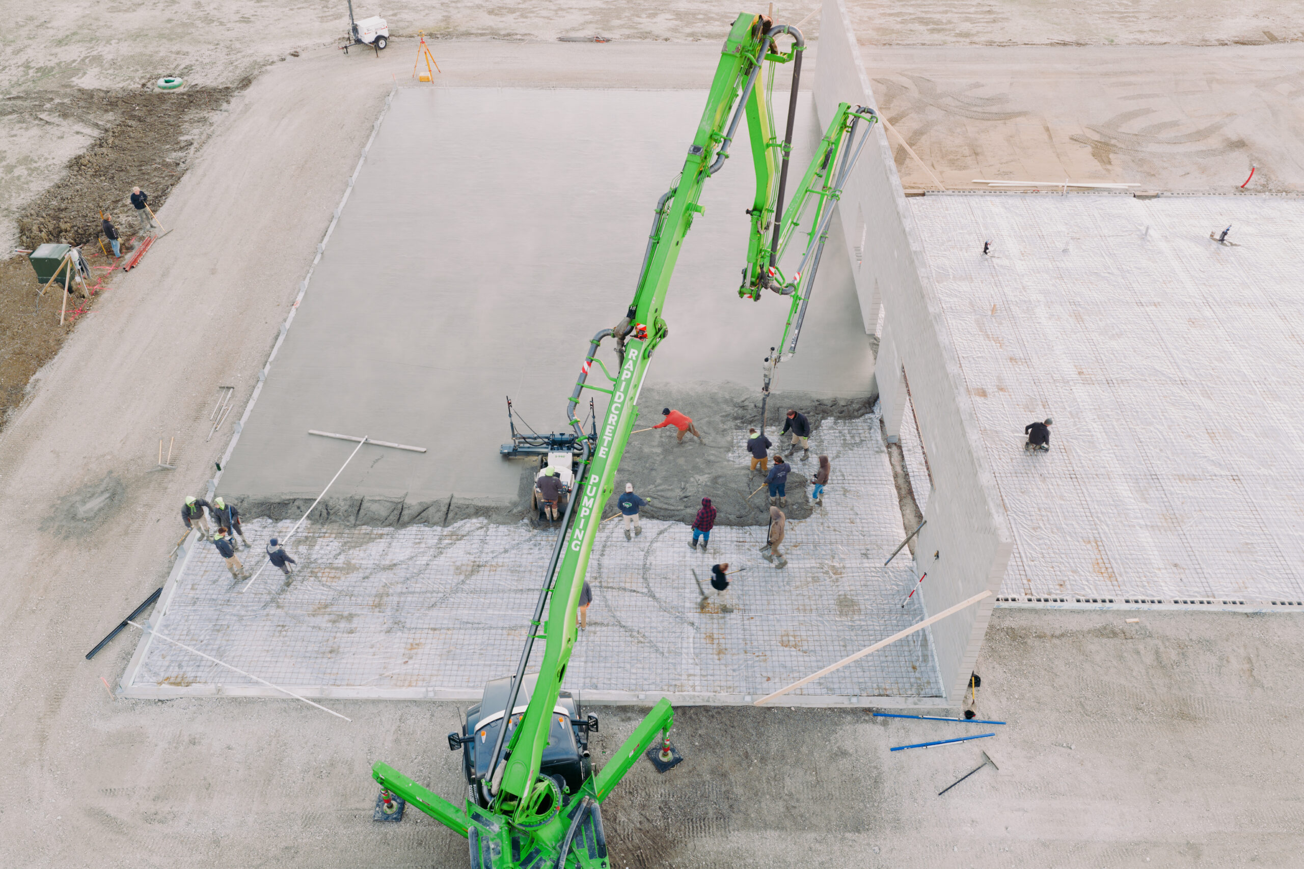Construction workers pour concrete on a building foundation with a green concrete pump.