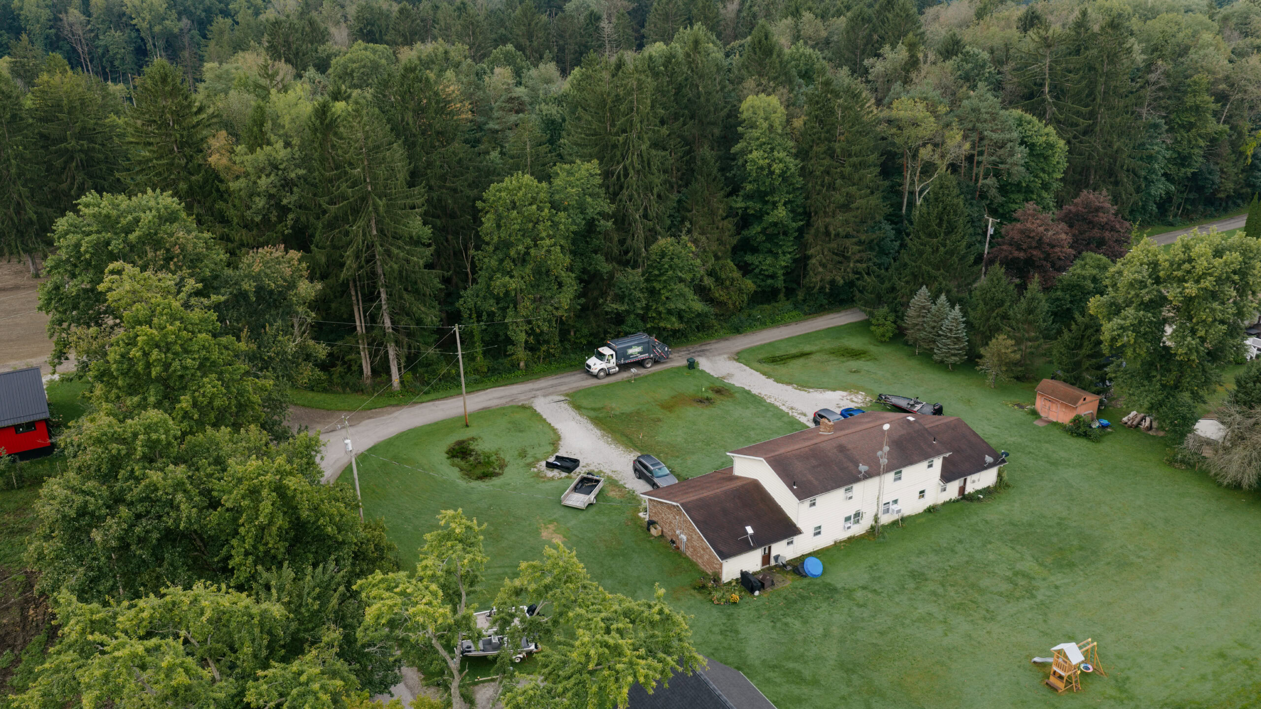 Aerial view of a rural property with a house, driveway, and surrounding trees.