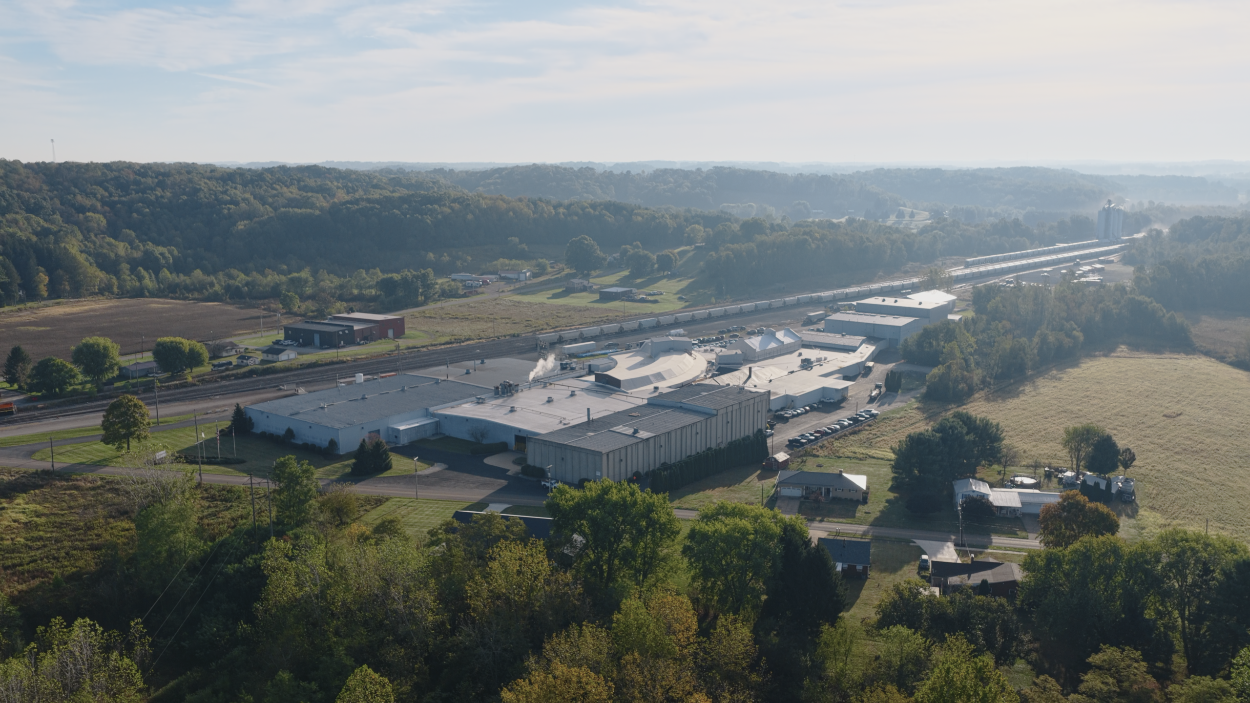Aerial view of a large industrial warehouse complex surrounded by greenery and fields.