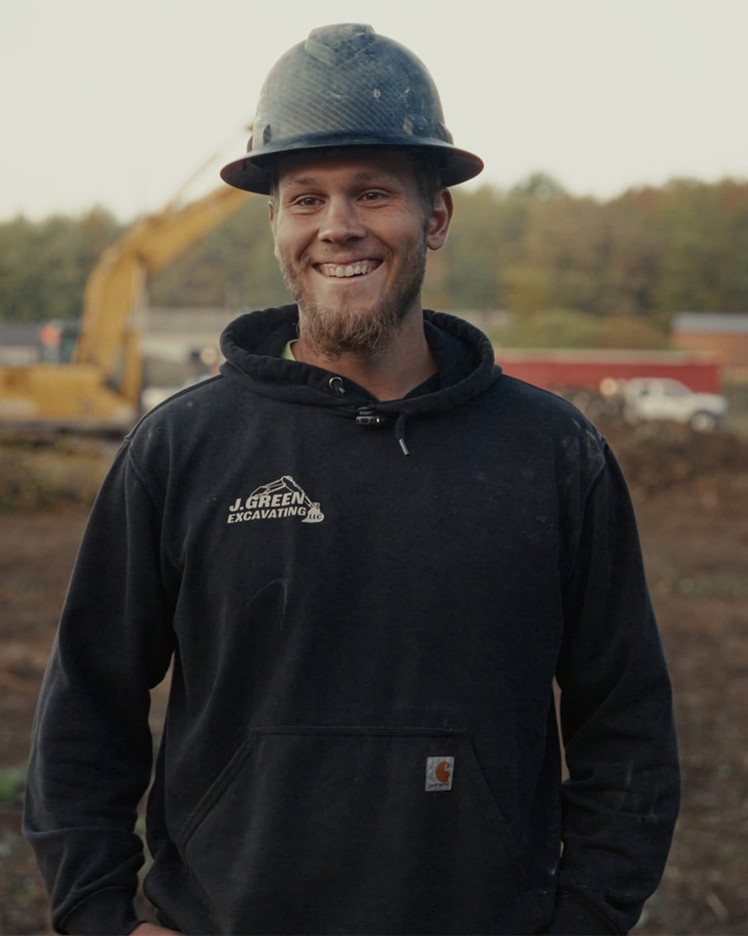 Construction worker in black hoodie and hard hat smiling at a Northeast Ohio construction site.